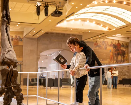 Young child standing with father looking up at a dinosaur skeleton.