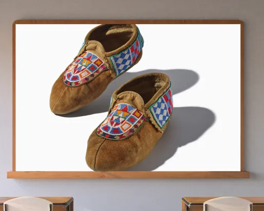 A screen in a classroom displays a pair of hide moccasins with colorful beading.