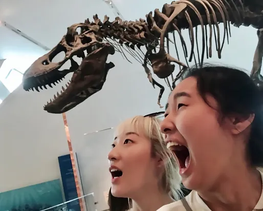 Two girls pretend to be scared in front of a T.rex skeleton