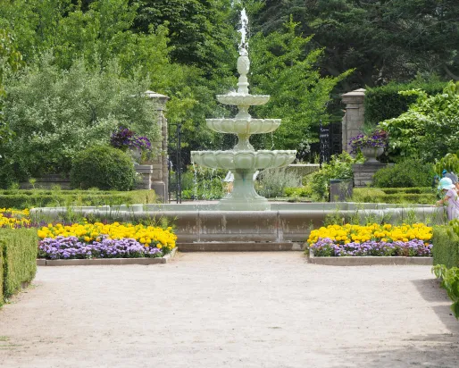 Fountain in background with flowers and walking path in foreground.