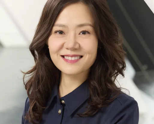 Portrait of a smiling woman with long wavy hair wearing a dark blue button-up shirt.