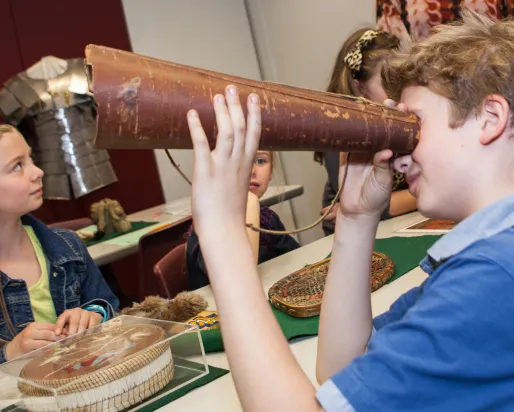 A student holds a birch bark moose call up to his eye while attempting to discern what it is.