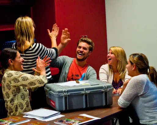 Teachers laugh and give each other high-fives around a table