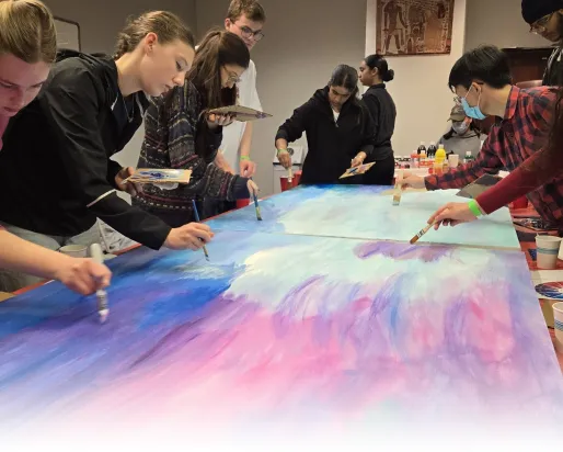 A group of Youth Cabinet members work together to paint a canvas with shades of blue, purple and pink.