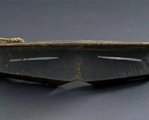Iggaak (snow goggles) carved from wood with narrow horizontal slits for the eyes, and a string at the back.