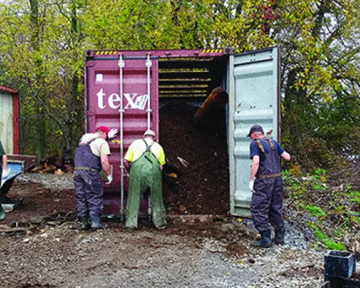 Trois hommes travaillent à côté d'un conteneur d'expédition contenant les os et le fumier de la baleine bleue.
