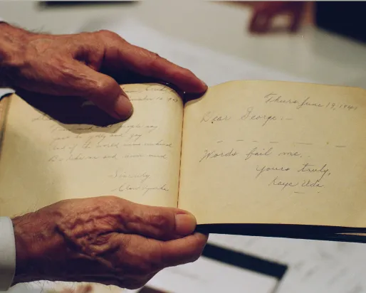Photo d'une paire de mains tenant un livre manuscrit. On peut y lire : "Cher George, les mots me manquent : Cher George, les mots me manquent. Bien à vous, Kaye Uda.
