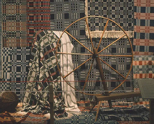 Photograph of textiles behind a spinning wheel
