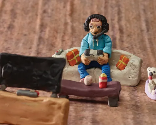 Detail of a diorama showing a person wearing headphones on a couch, playing a video game while looking at a television screen.