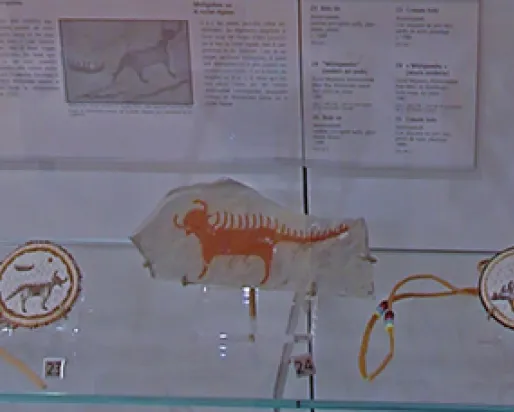 A display of art, including two beaded medallions and a painting on rock, inspired by the pictographs at Agawa Rock. The spirit depicted in the art is four-legged with horns and a long tail. It has spikes running down the length of its back and tail.
