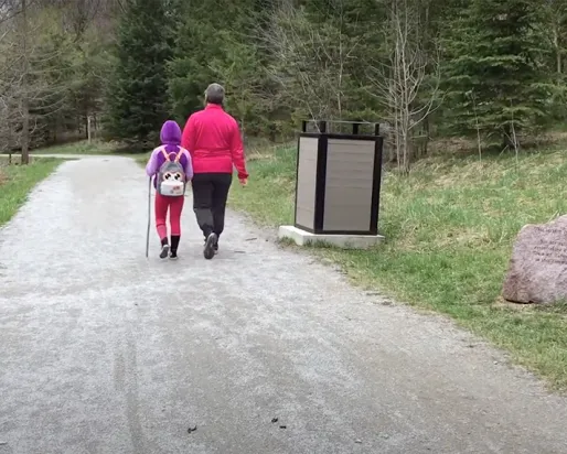 Woman and child walking along a trail path into a forest.
