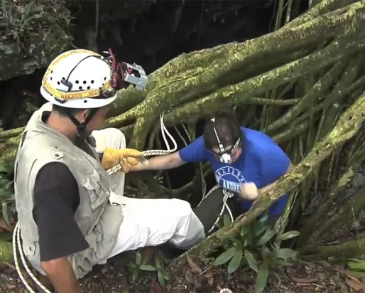 Un homme aide une femme à descendre le long d'une corde dans l'ouverture d'une grotte dans la jungle.