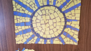  Mosaic of a sun made from yellow, blue, and black squares.