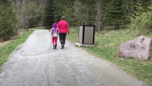 A woman and child walk down a gravel path on a nature trail through the forest.