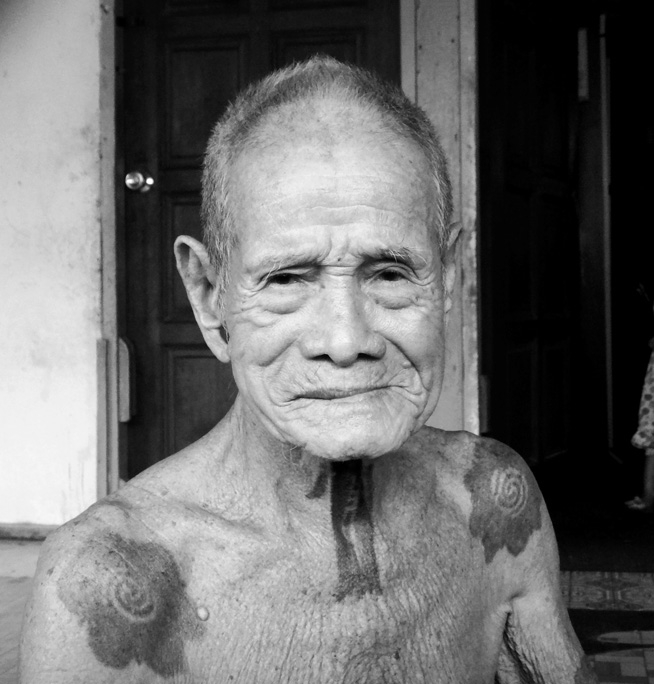 Black and white photograph of an older man with tattoos on his neck and shoulders