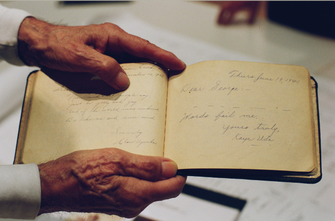 Photo of a pair of hands holding a handwritten book. The entry reads: Dear George, Words fail me. Yours truly, Kaye Uda.