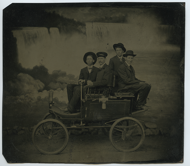 Black and white tintype photo of four men sitting on a cart in front of Niagara Falls