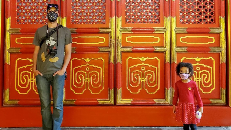 A masked adult and child in front of the Chinese imperial temple at ROM.