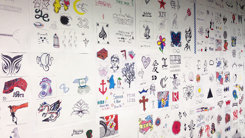 Hundreds of tattoo designs on white paper are posted on a wall
