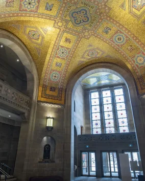 The ceiling of the ROM Rotunda the gold tiles shimmer in the light coming through the stain glass window.