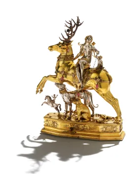 A silver woman sits on top of a golden stag, below her are dogs and another person riding a horse.