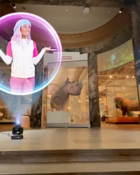 A holographic projection of ECO, the Earth Rangers Communications Operative with colorful hair and a white and pink outfit, appears inside a glowing orb at the Royal Ontario Museum entrance, where she shares engaging lessons about biodiversity and wildlife conservation with visitors.