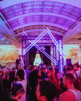 A crowd in a museum conversing. In the background is a DJ under a disco ball.
