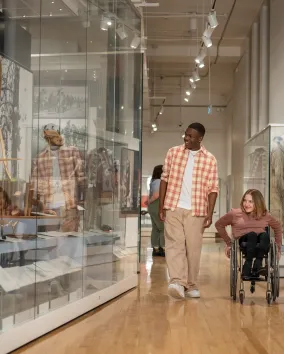 A guy in a plaid shirt walking with a girl in a wheelchair looking at museum collections at ROM
