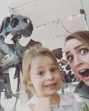 A young woman and a child pretend to be scared in front of a T.rex skeleton