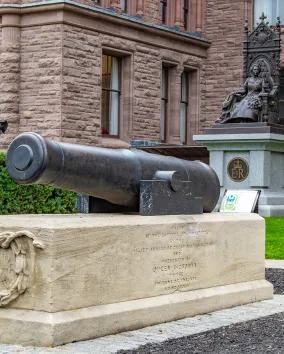 Canon in foreground with statue and building in background