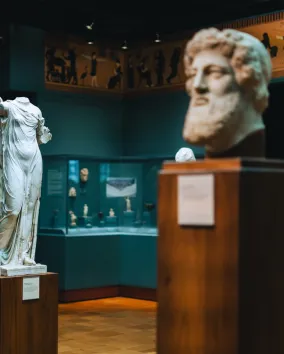 Ancient Greek statues and marble reliefs displayed in a museum gallery.