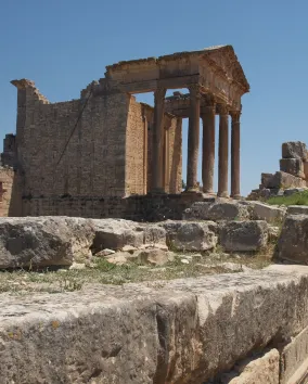 The ruins of an ancient temple with weathered columns and a clear blue sky in the background