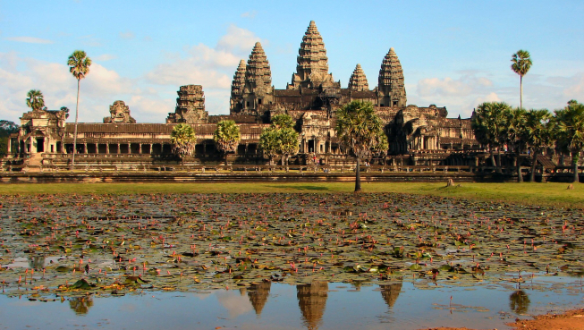 A large temple complex with towers and trees and a moat in the foreground.