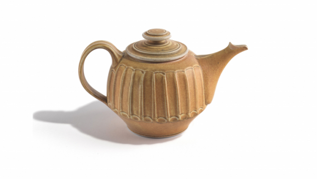 Mustard-peach coloured ceramic, wheel thrown teapot and lid on a white background.