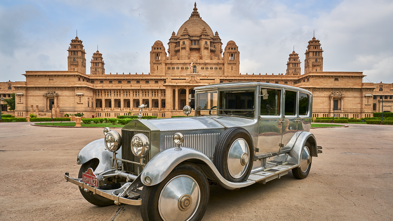 Une Rolls-Royce Phantom 1927 devant une opulente résidence ornée de colonnades et coiffée d'un dôme.