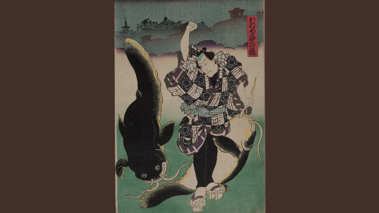 An actor dressed as Fuku of Kaname-ishi stands, grasping the barbel of a large, subdued catfish in one hand, and raising his other fist to strike a second large catfish.