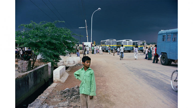 Boy standing on a dirt road near a bus stop