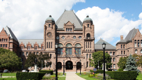 L’Assemblée législative de l’Ontario, un édifice massif en pierre de style roman richardsonien couronné d'un toit à pic.