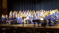La St. Mary’s Memorial High School Choir sur scène. Environ une centaine de personnes vêtues de robes, en plus d'une pianiste et d'une chef d'orchestre.