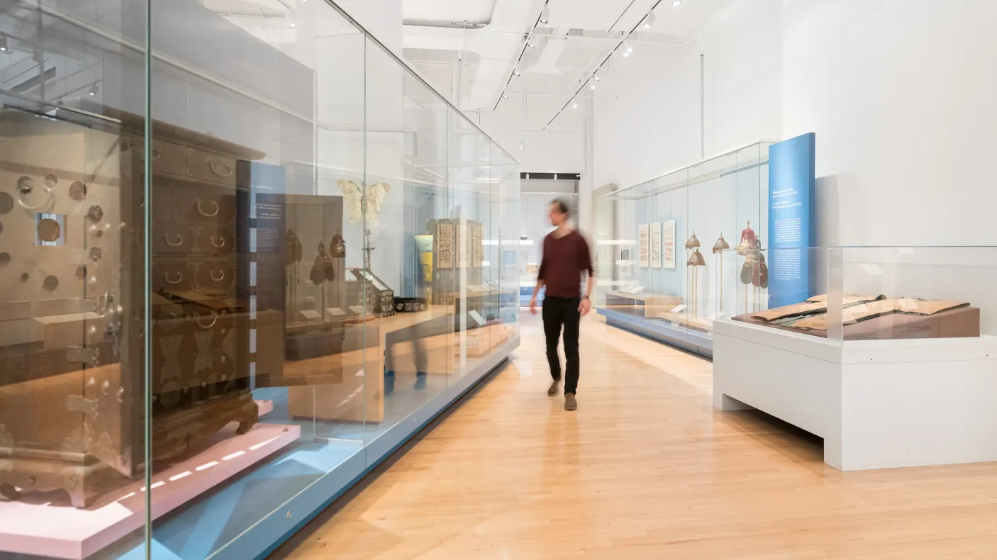 A person walks through a gallery admiring the large furniture in glass cases/