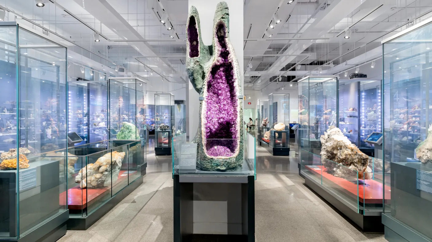 A gallery filled with minerals and gems in the centre there is a very large quartz variety amethyst geode.