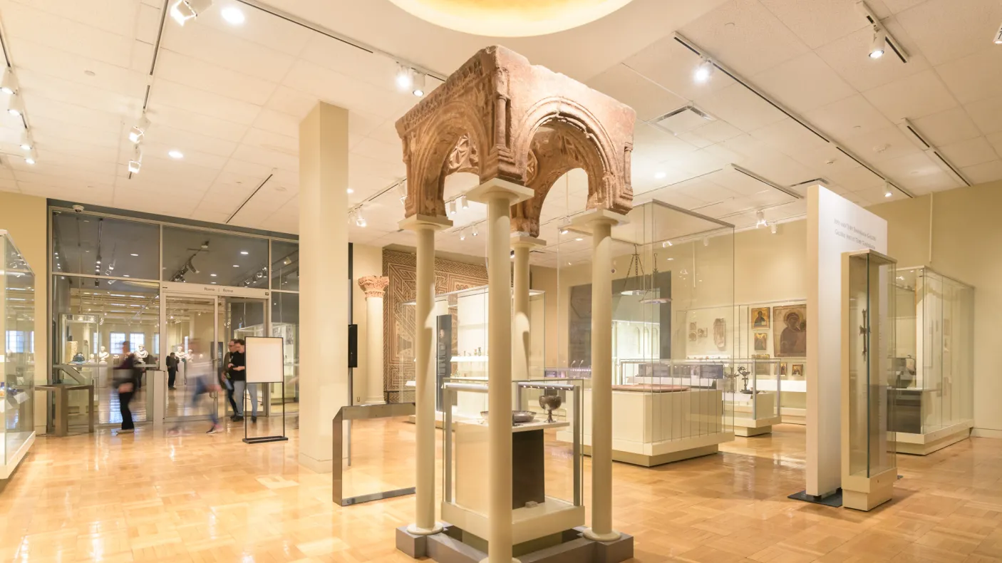An ancient archway supported by modern pillars above a case containing a goblet and bowl.