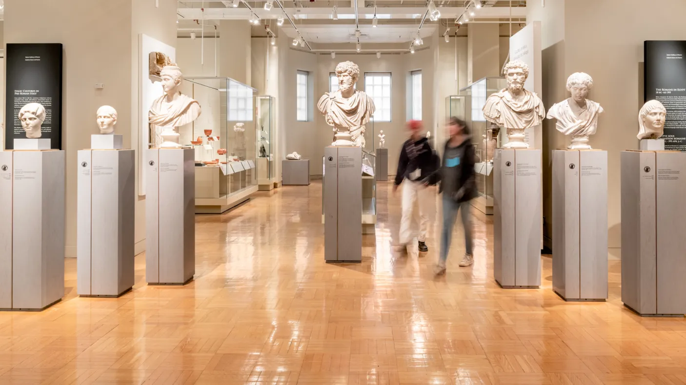Two people walk among the marble busts of important Romans.