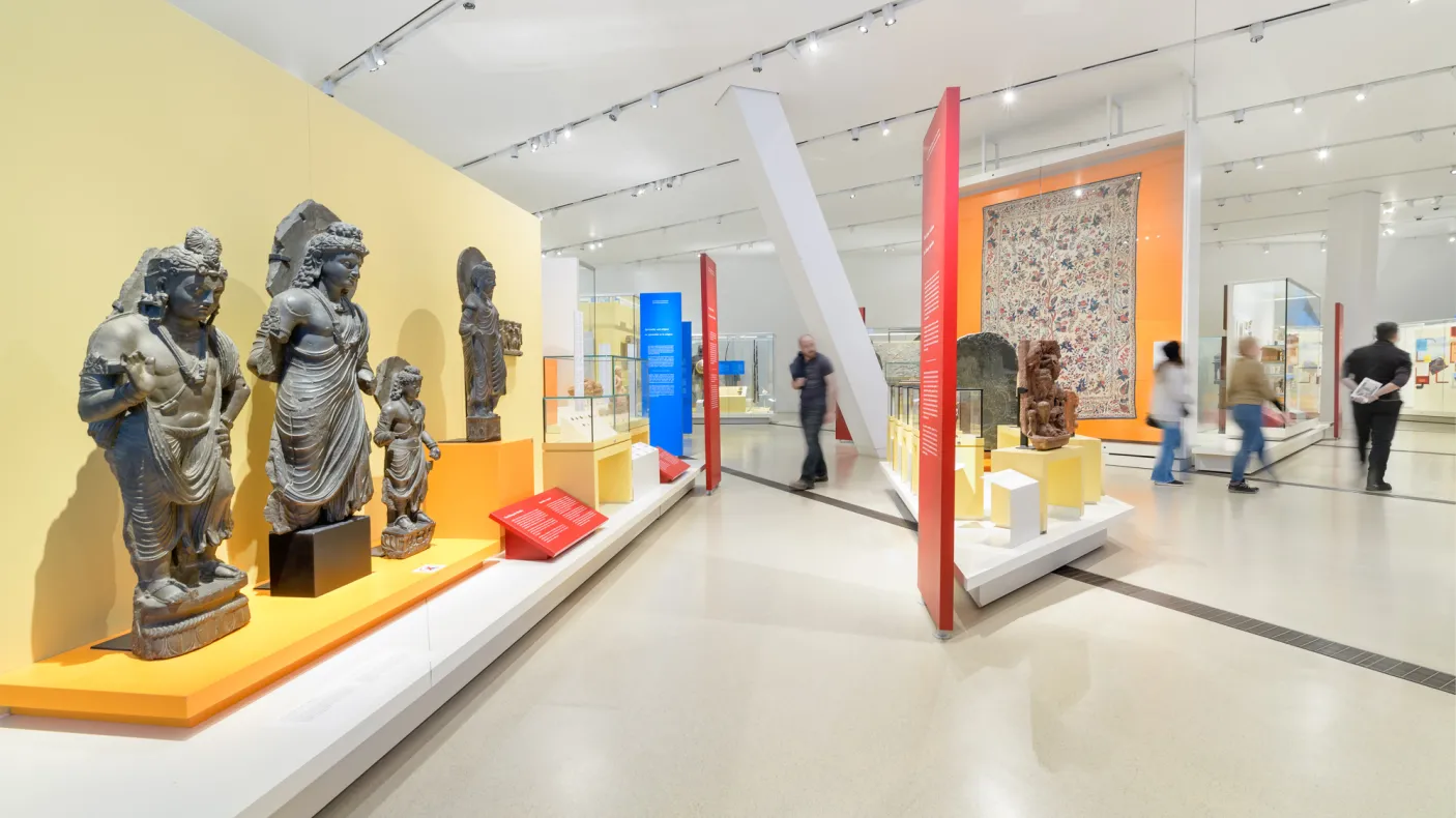 People walk around a gallery featuring statues of South Asian religious figures.