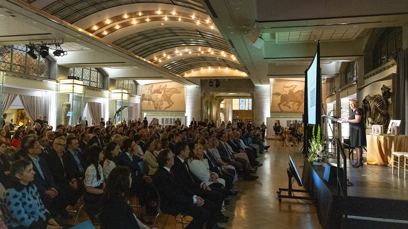 Audience of people seated, listening to a speaker on stage