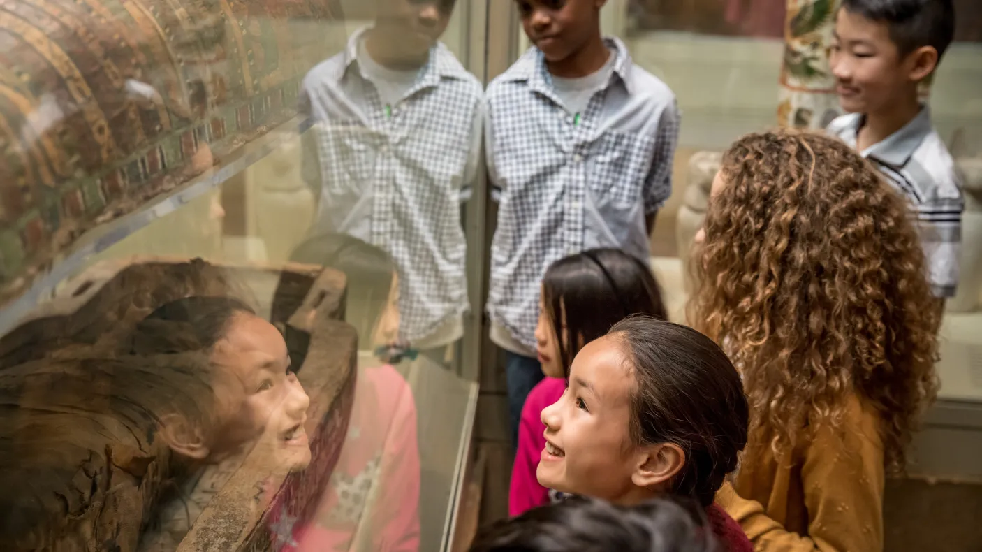 Children looking at an ancient Egyptian mummy display in a museum exhibit.