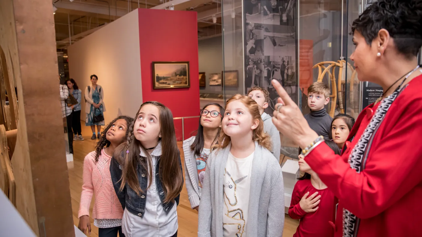 A group of children listens to a guide explaining an exhibit.