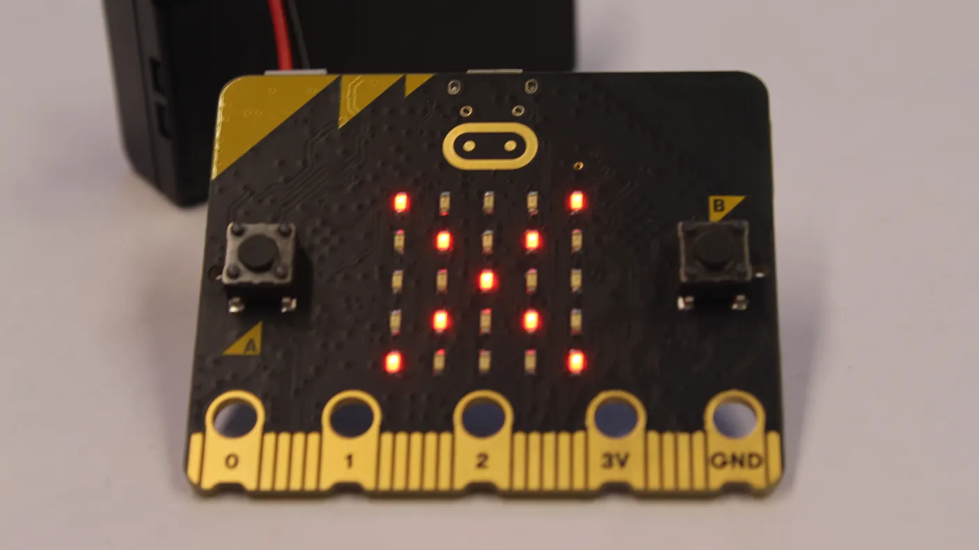A black MicroBit displays illuminated LEDs in the form of an X