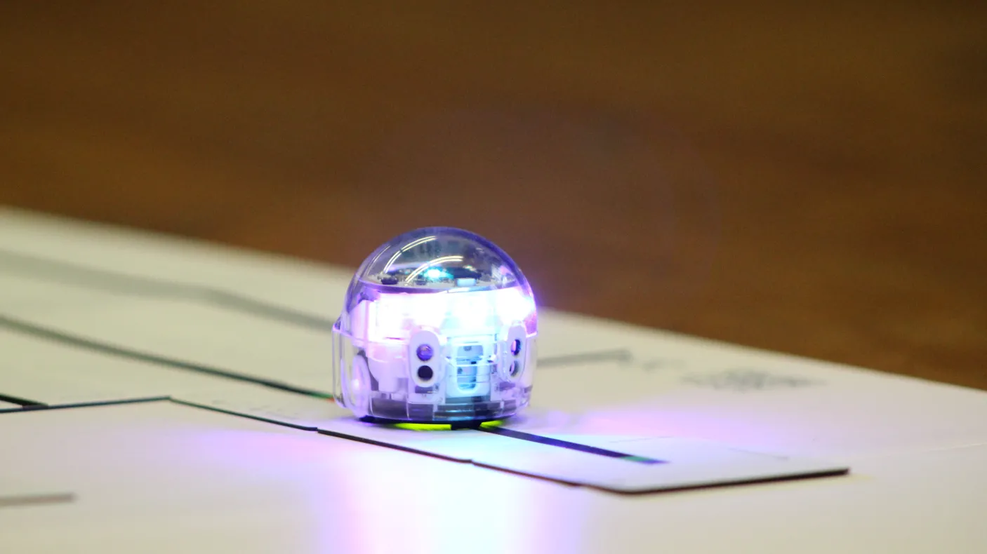 A small silver robot rolls along a dark track on a paper