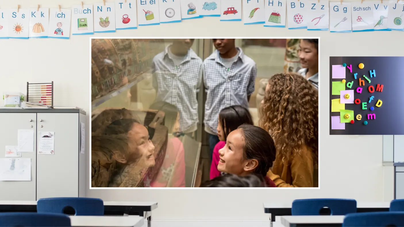A screen in a classroom shows a scene of smiling students gathered around a museum case holding a mummified Ancient Egyptian